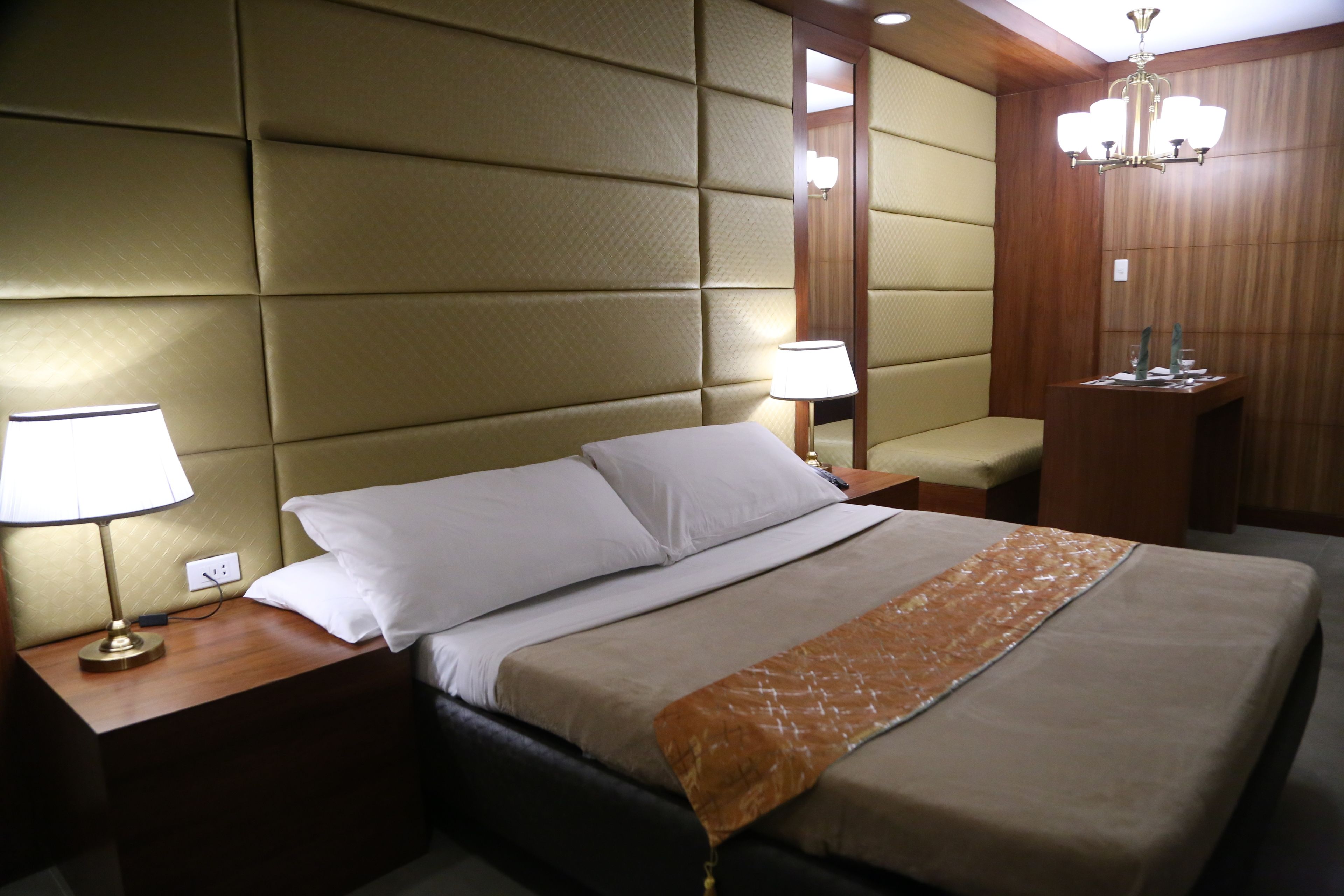 A hotel room with a large bed, two bedside tables with lamps, a wooden nightstand, and a mirror.