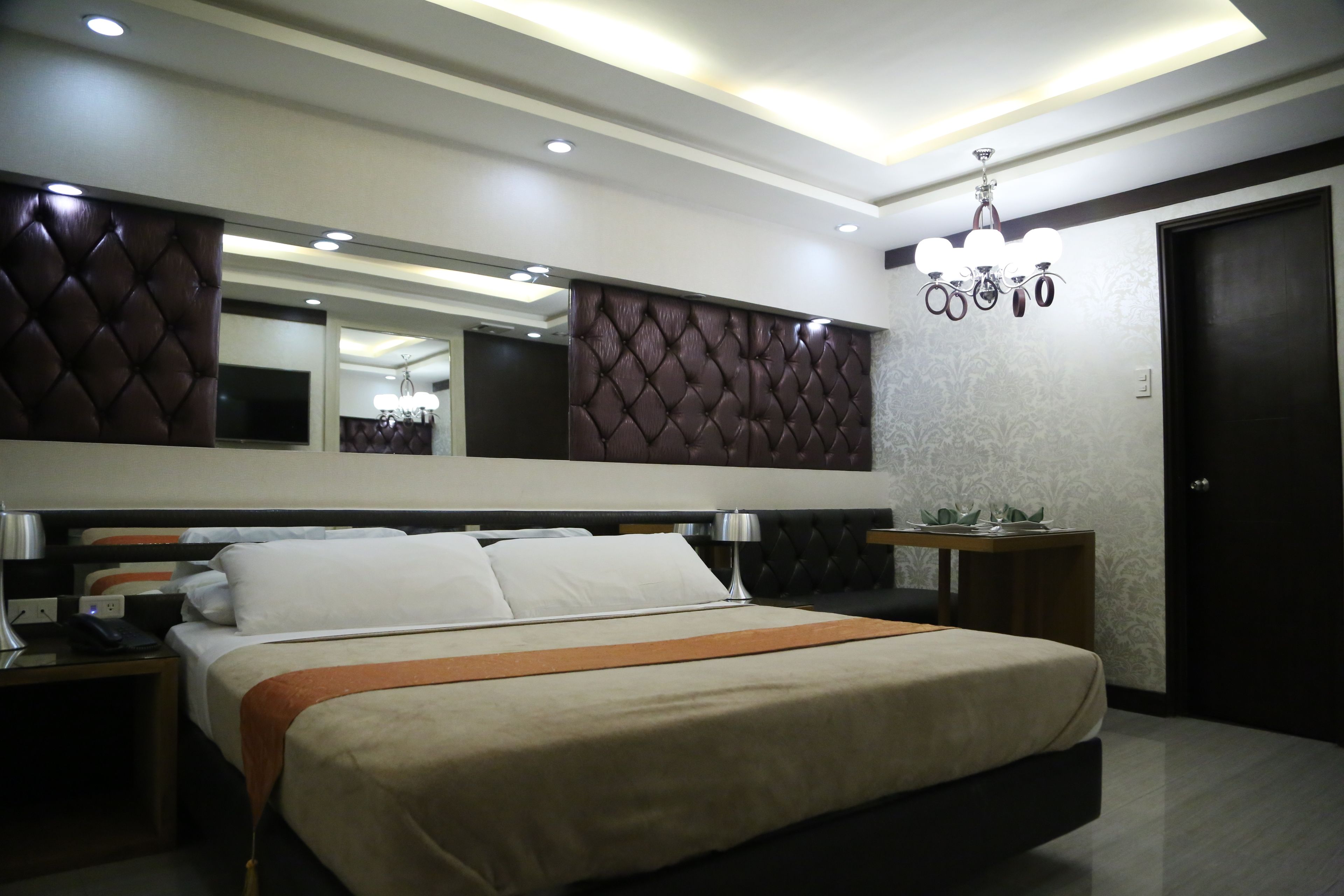 Une chambre d’hôtel moderne avec un grand lit, une table de chevet, un bureau, un miroir et un lustre.