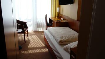 Ein Hotelzimmer mit Bett, Schreibtisch, Sessel, einem an der Wand montierten Fernseher und einem Fenster mit Vorhängen.
