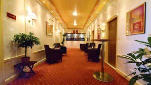 Un corridoio d'hotel con tappeto rosso, piante in vaso e zone relax.