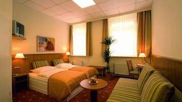 A hotel room with two beds, a sofa, a small table, a potted plant, and a painting on the wall.