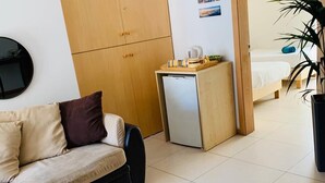 A modern living room with a sofa, a small wooden cabinet, a refrigerator, and a bed in the background. - Hostel Malti (St. Julian's)