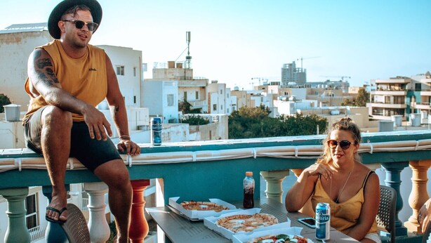 A rooftop terrace with a table set for two, pizza boxes, and a can of beer. - Hostel Malti (St. Julian's)