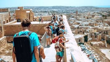 A group of people on a stone pathway overlooking a cityscape with buildings and a distant view of the sea.