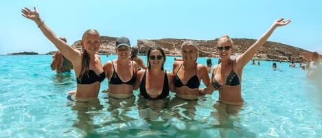 A group of people in a clear blue pool with rocky hills in the background.