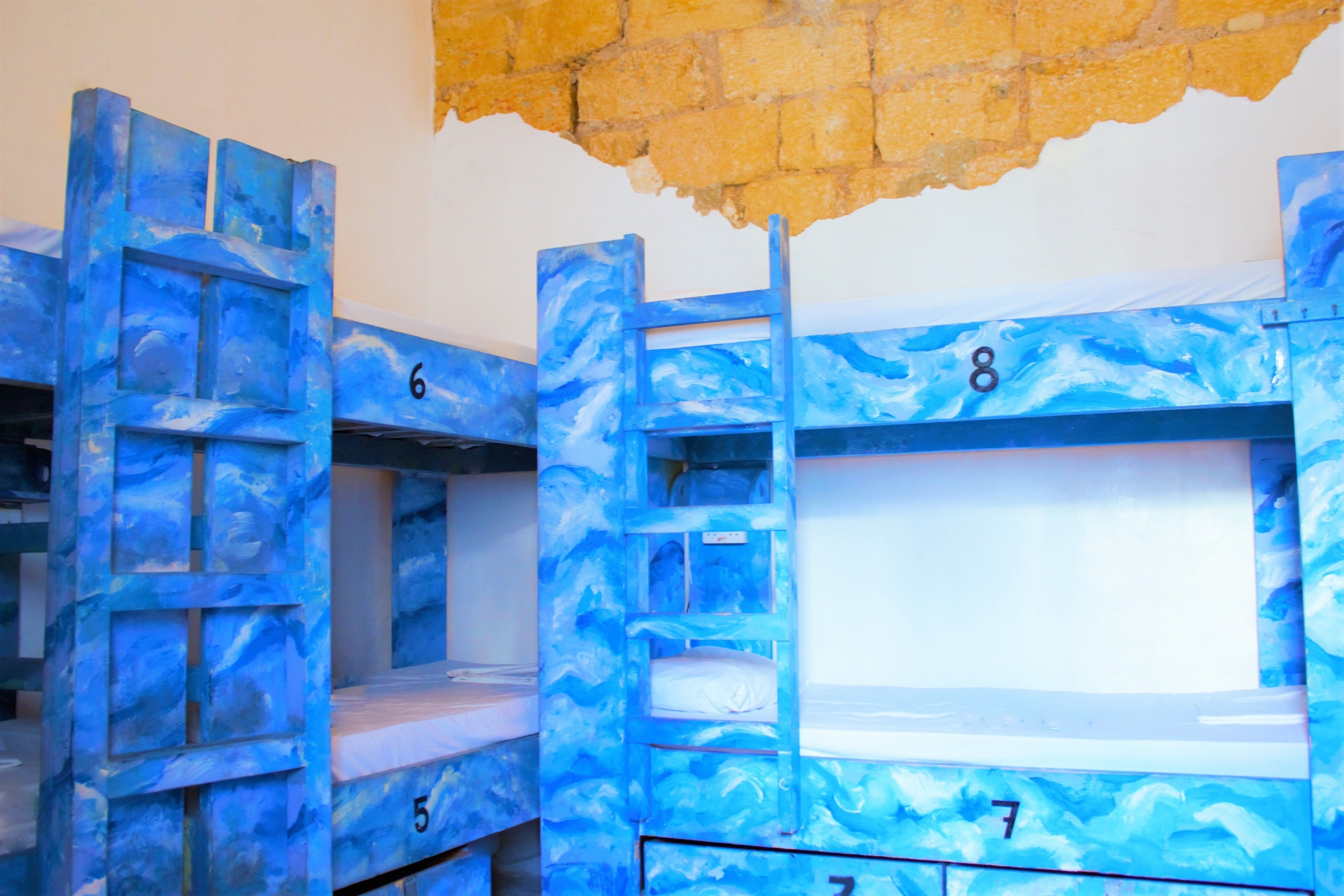 Bunk beds with numbers 5, 6, 7, and 8, in a room with a brick wall and a window.