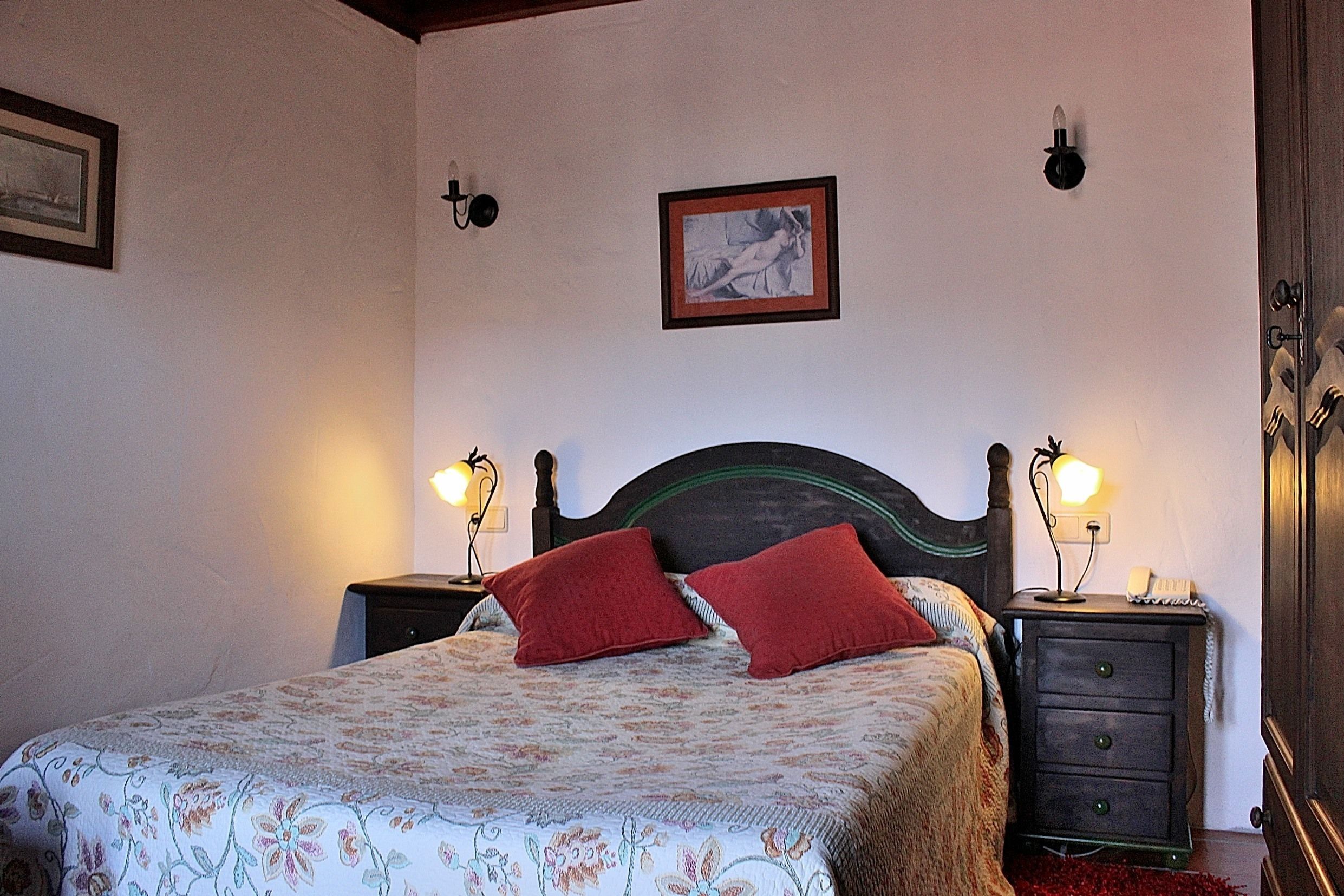 A bedroom with a bed, two bedside tables, a nightstand, a framed picture on the wall, and a wooden wardrobe.