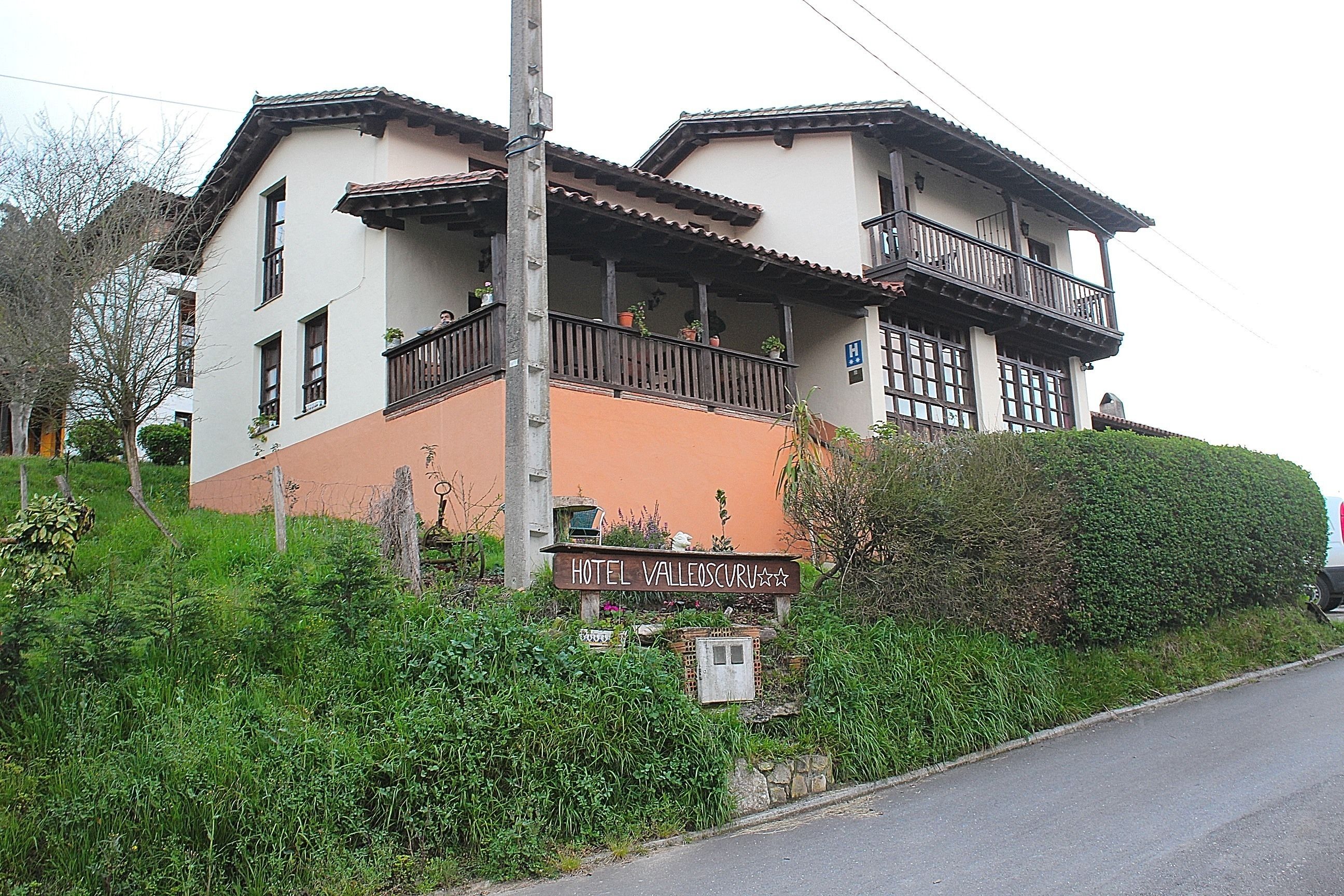 A two-story hotel with balconies, a sign indicating it is a hotel, and a view of the surrounding greenery.