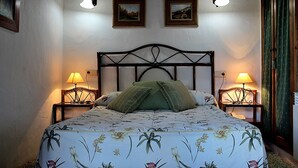 Una cama bien hecha con ropa de cama floral, dos lámparas de noche y cuadros en la pared.