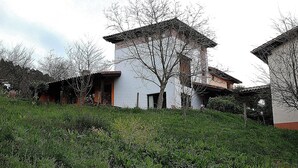 Un edificio con fachada blanca y tejado rojo, rodeado de vegetación y árboles.