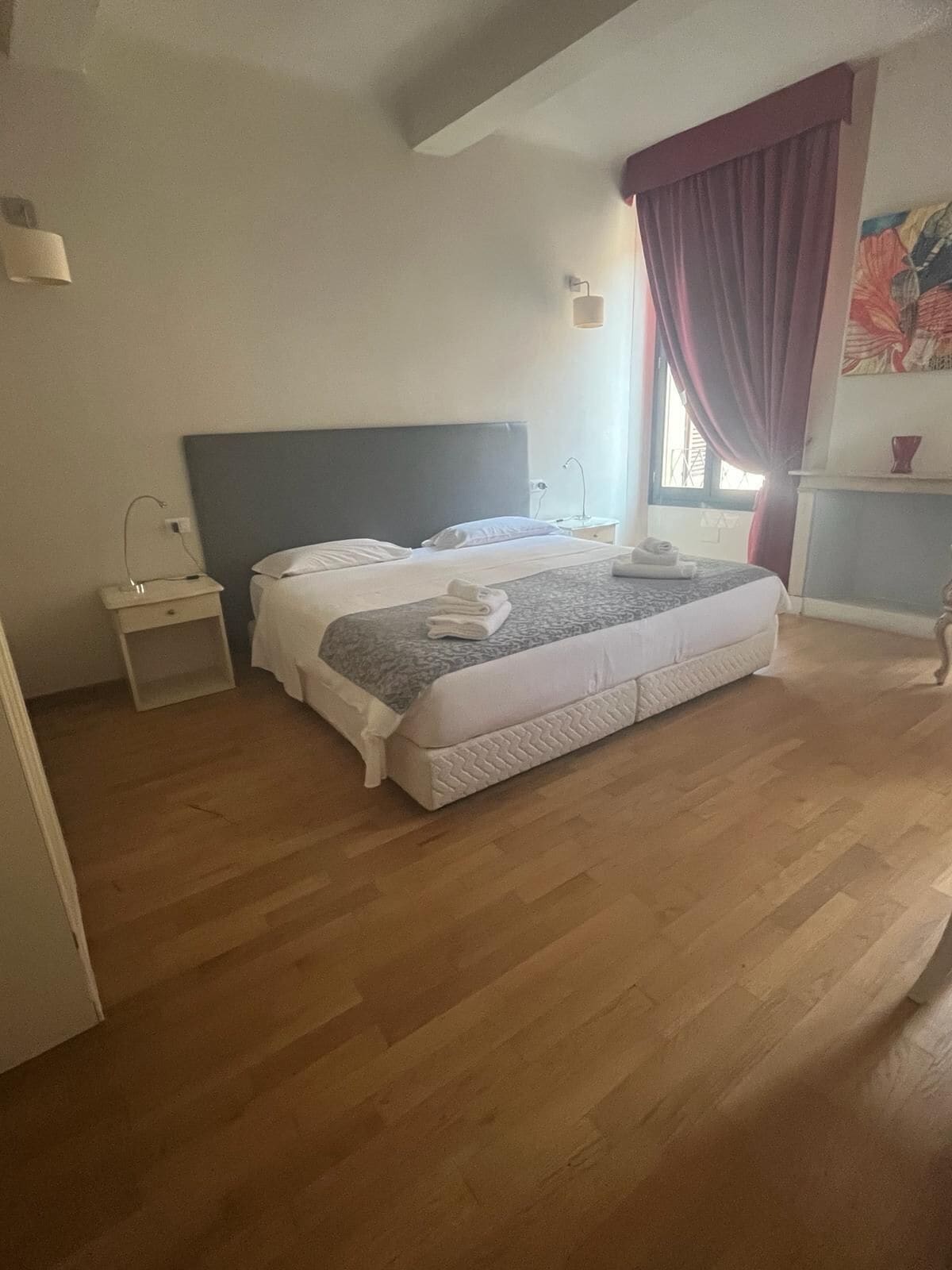 A bedroom with a bed, nightstands, a window with curtains, and a painting on the wall.
