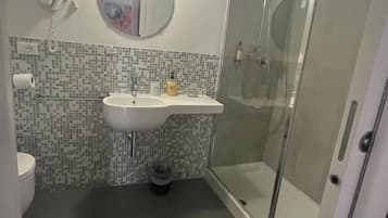 Un baño con piso de baldosas, un lavamanos con espejo, un inodoro y una ducha con mampara de vidrio.