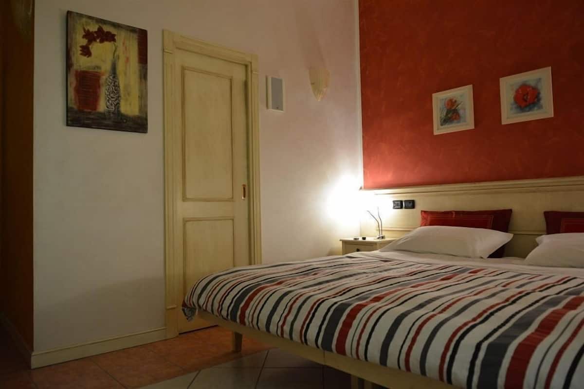A bedroom with a bed, a nightstand, a lamp, and two paintings on the wall.