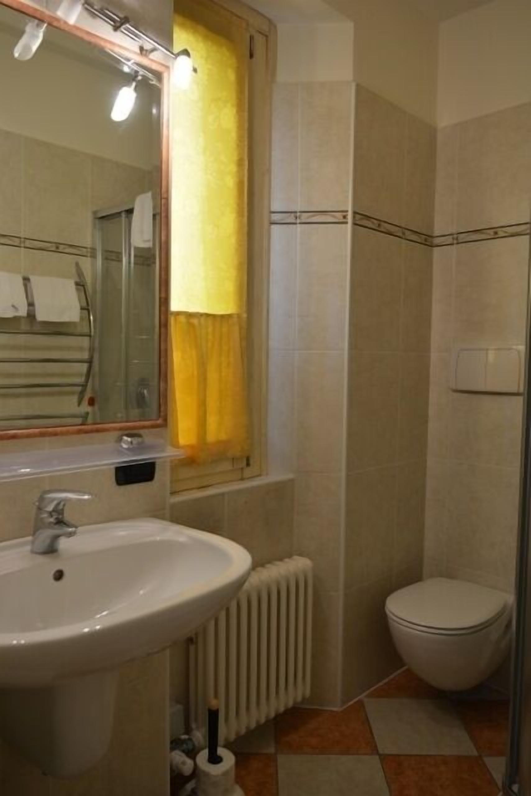 A bathroom with a sink, mirror, toilet, and a window with a yellow curtain.
