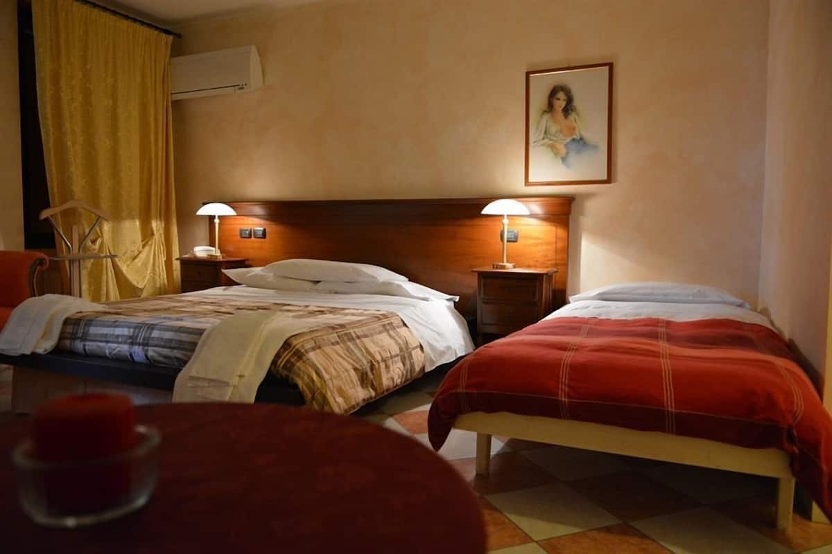 A hotel room with two beds, each with a lamp, a painting on the wall, and a chair by the window.