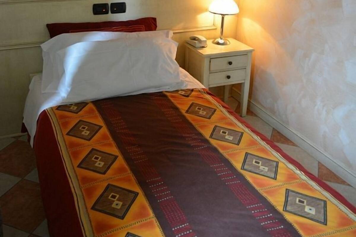 A hotel room with a bed, a nightstand with a lamp, and a wall-mounted picture.