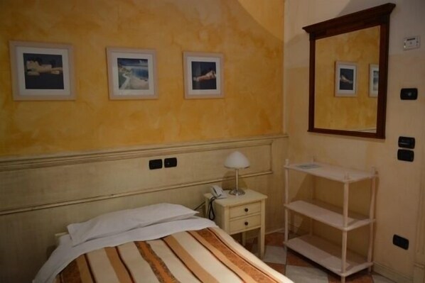 Habitación de hotel con cama, mesita de noche con lámpara, espejo y tres cuadros en la pared.