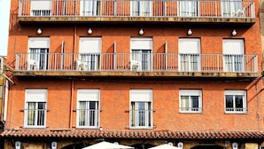 Un edificio de varios pisos con balcones, una cafetería a nivel de calle con terraza, y una entrada visible.