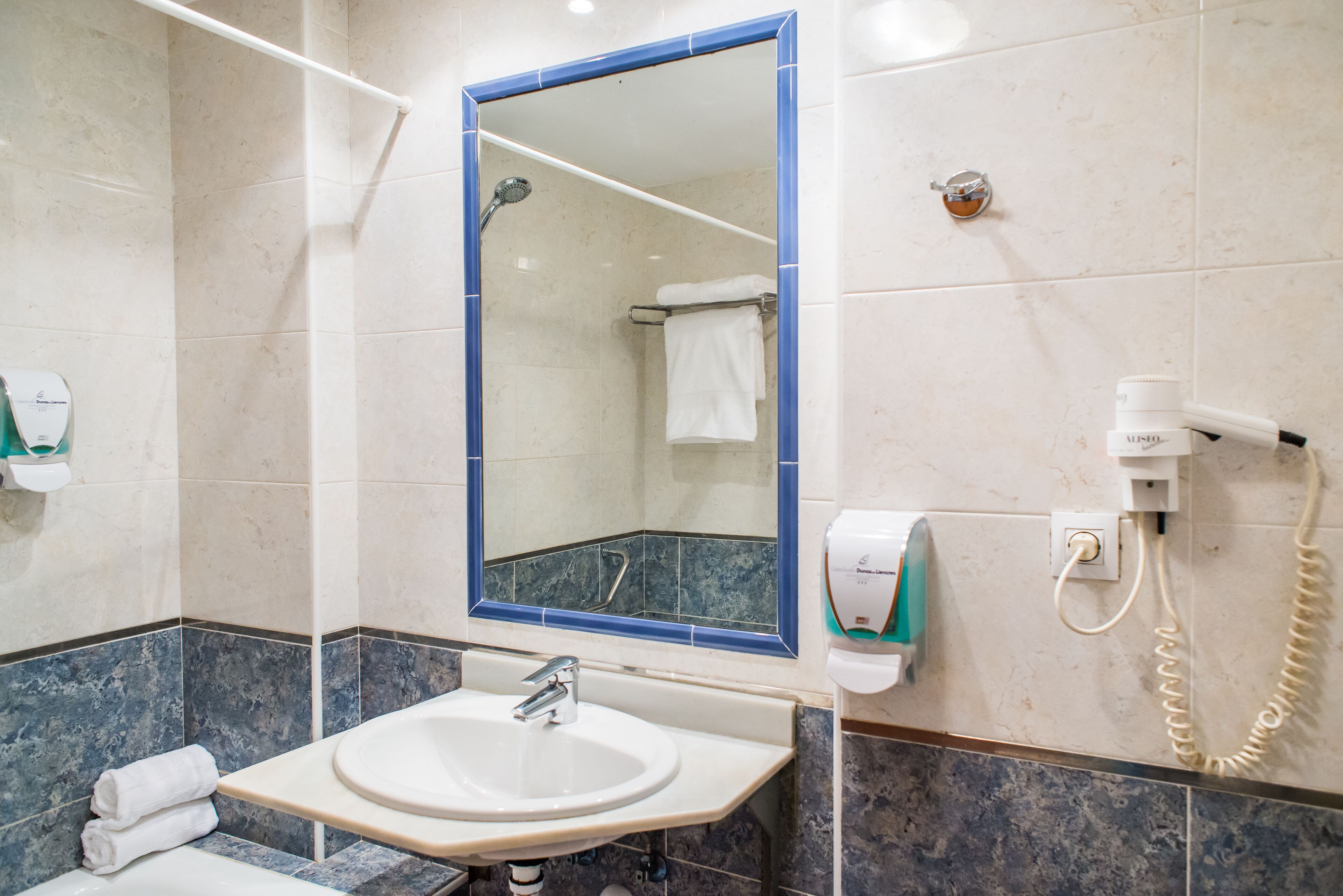 A bathroom with a sink, mirror, towel rack, and a hand dryer.