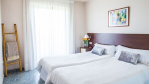 A hotel room with two beds, a wooden ladder, a nightstand with a lamp and flowers, and a painting on the wall.