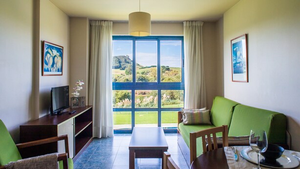 A room with a large window, a green sofa, a wooden table, and a television on a stand.