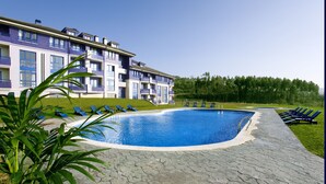 A swimming pool with lounge chairs, a building with balconies, and a grassy area.
