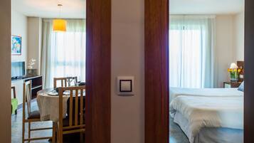 Una habitación de hotel con cama, zona de comedor con sillas y mesa, y ventana con cortinas.