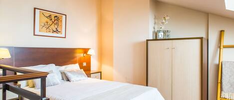A hotel room with a bed, bedside table, lamp, wardrobe, and a framed artwork on the wall.