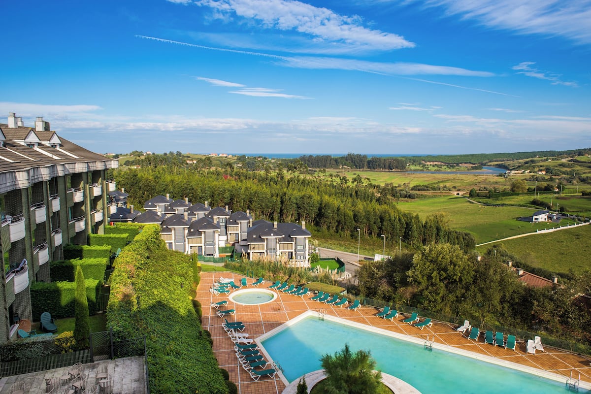 Een hotel met een zwembad, ligbedden en uitzicht op het omliggende landschap.