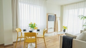 A modern living room with a dining area, wooden flooring, and a flat-screen TV mounted on the wall. - Aparthotel Playas de Liencres (Pielagos)