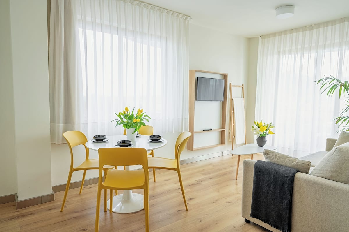 Een moderne woonkamer met een eethoek, houten vloeren en een flatscreen televisie aan de muur.