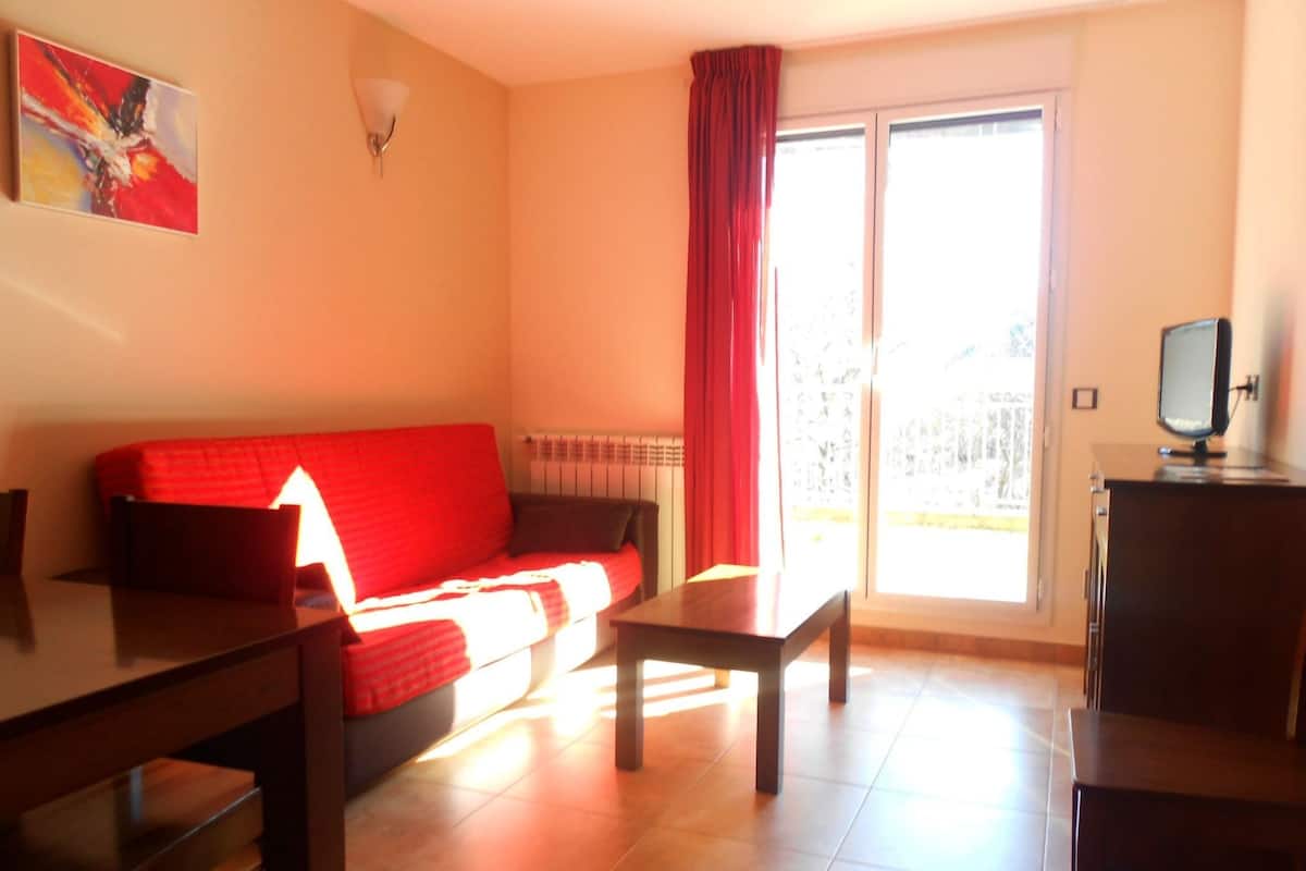 A living room with a red sofa, a wooden table, and a TV on a cabinet.