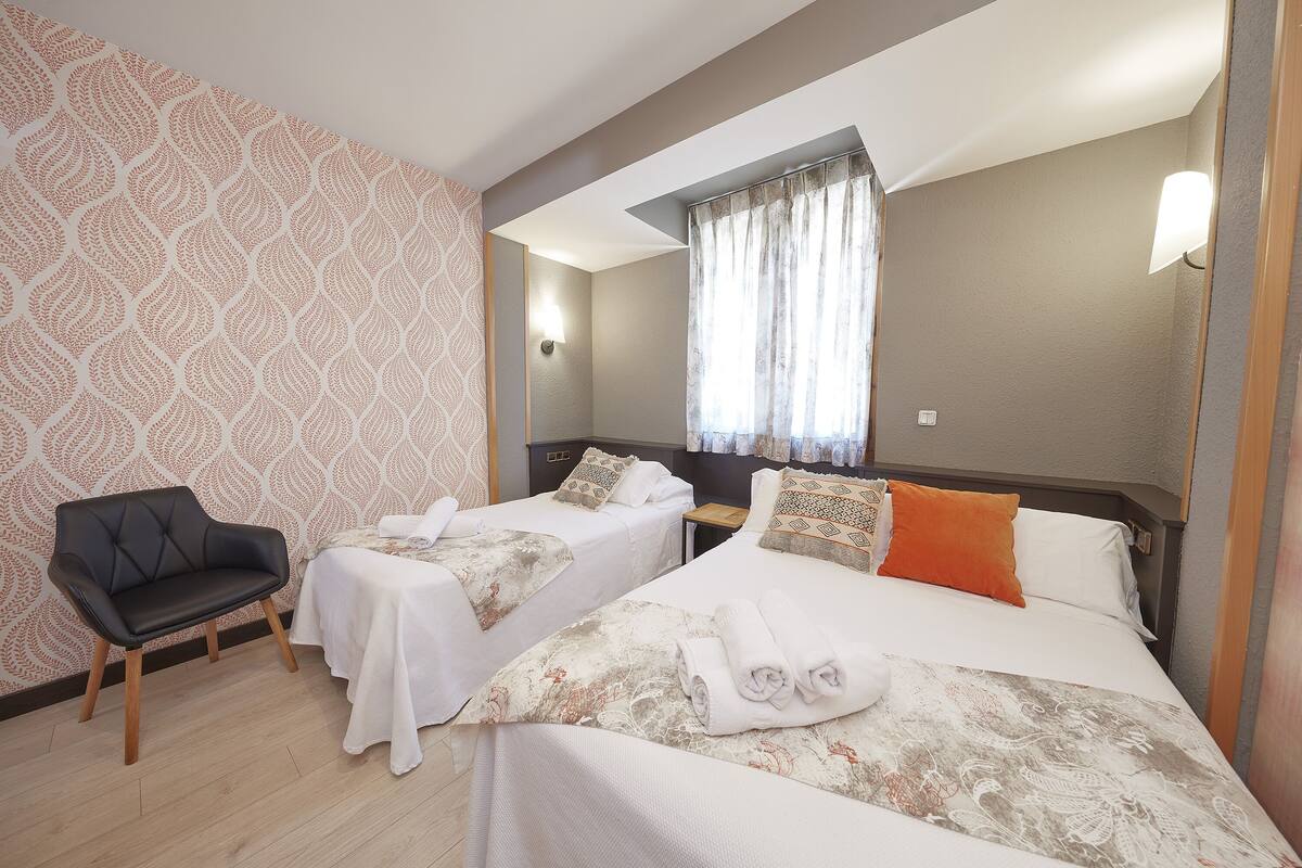 A hotel room with two beds, a chair, and a window with curtains.