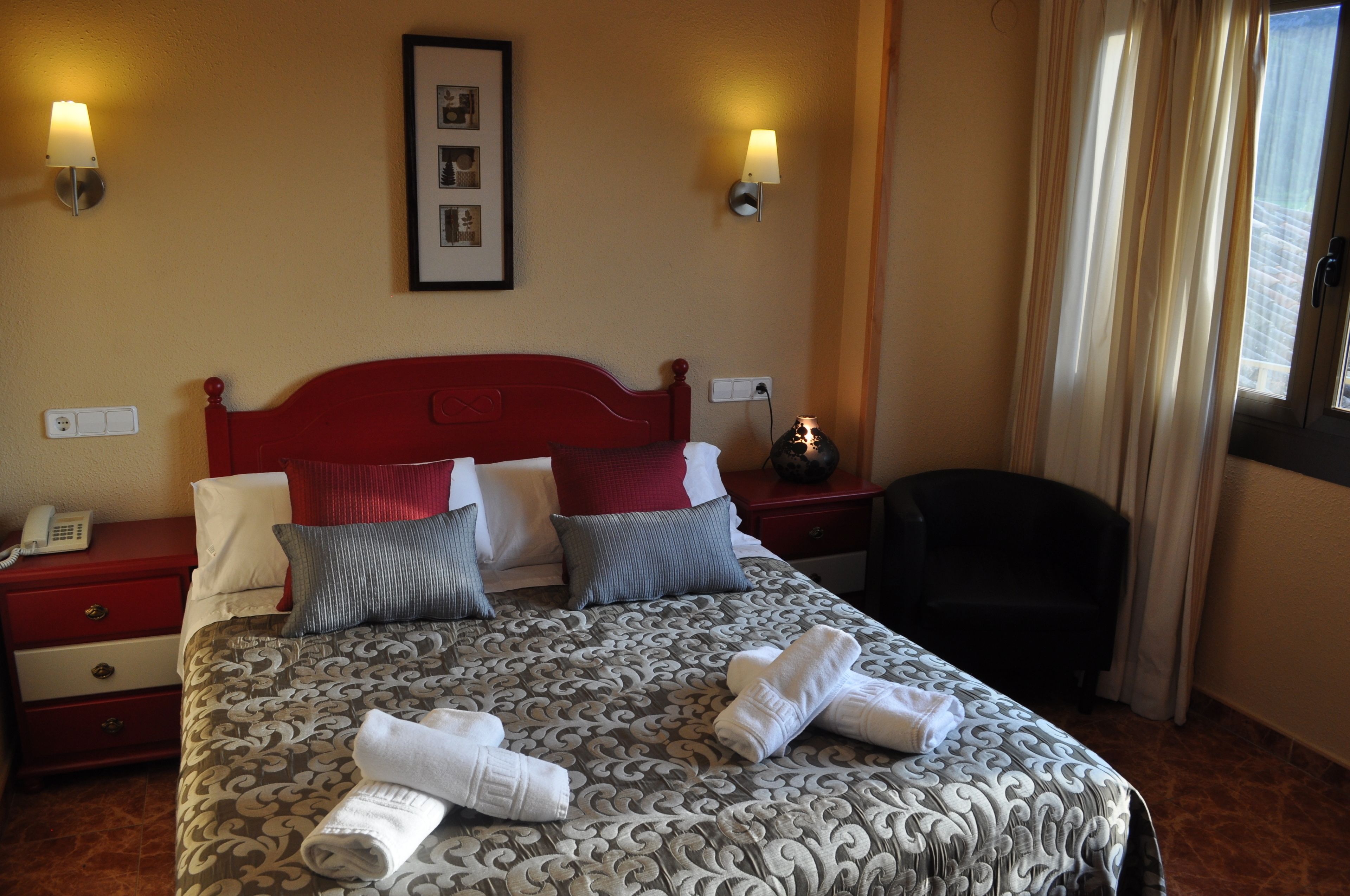 Een hotelkamer met een groot bed, twee nachtkastjes, een stoel en een raam met gordijnen.