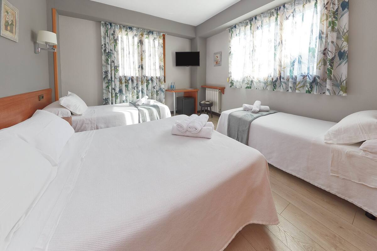 A hotel room with two beds, a desk, a chair, a TV, and a window with curtains.