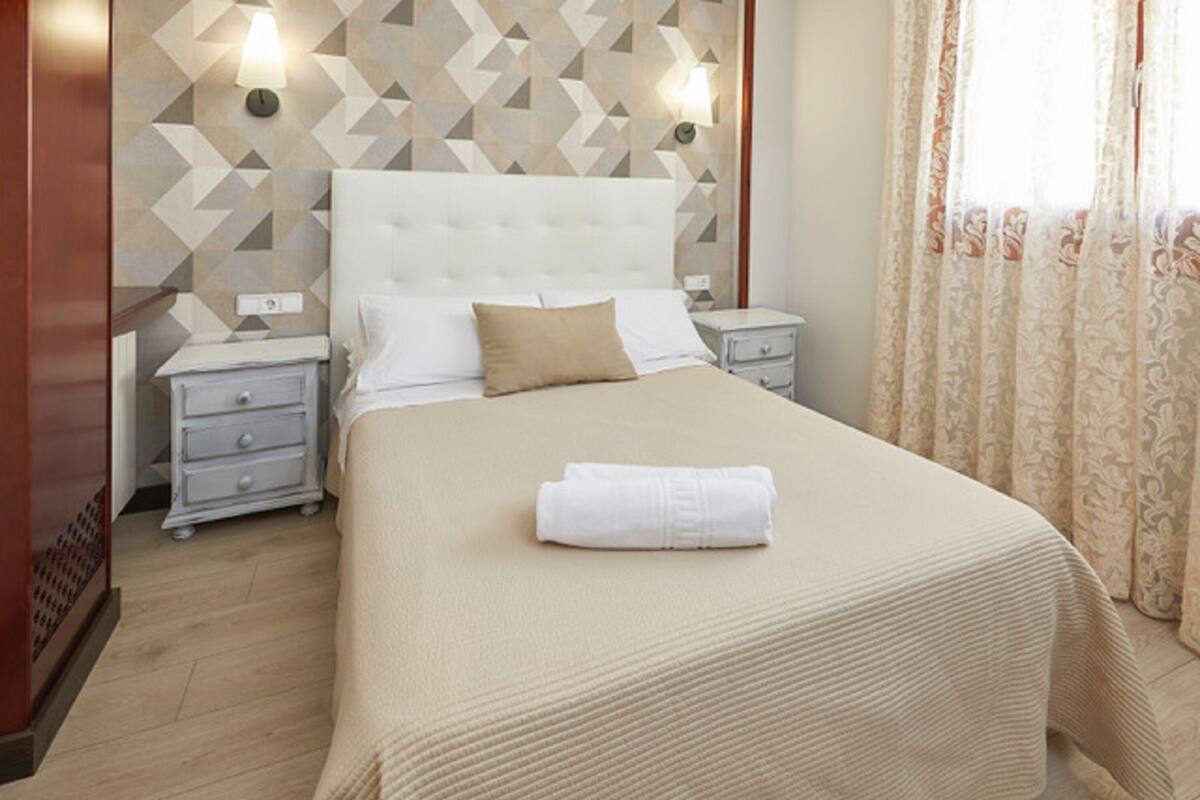 A neatly made bed with a folded towel, a white headboard, and a geometric-patterned wall.