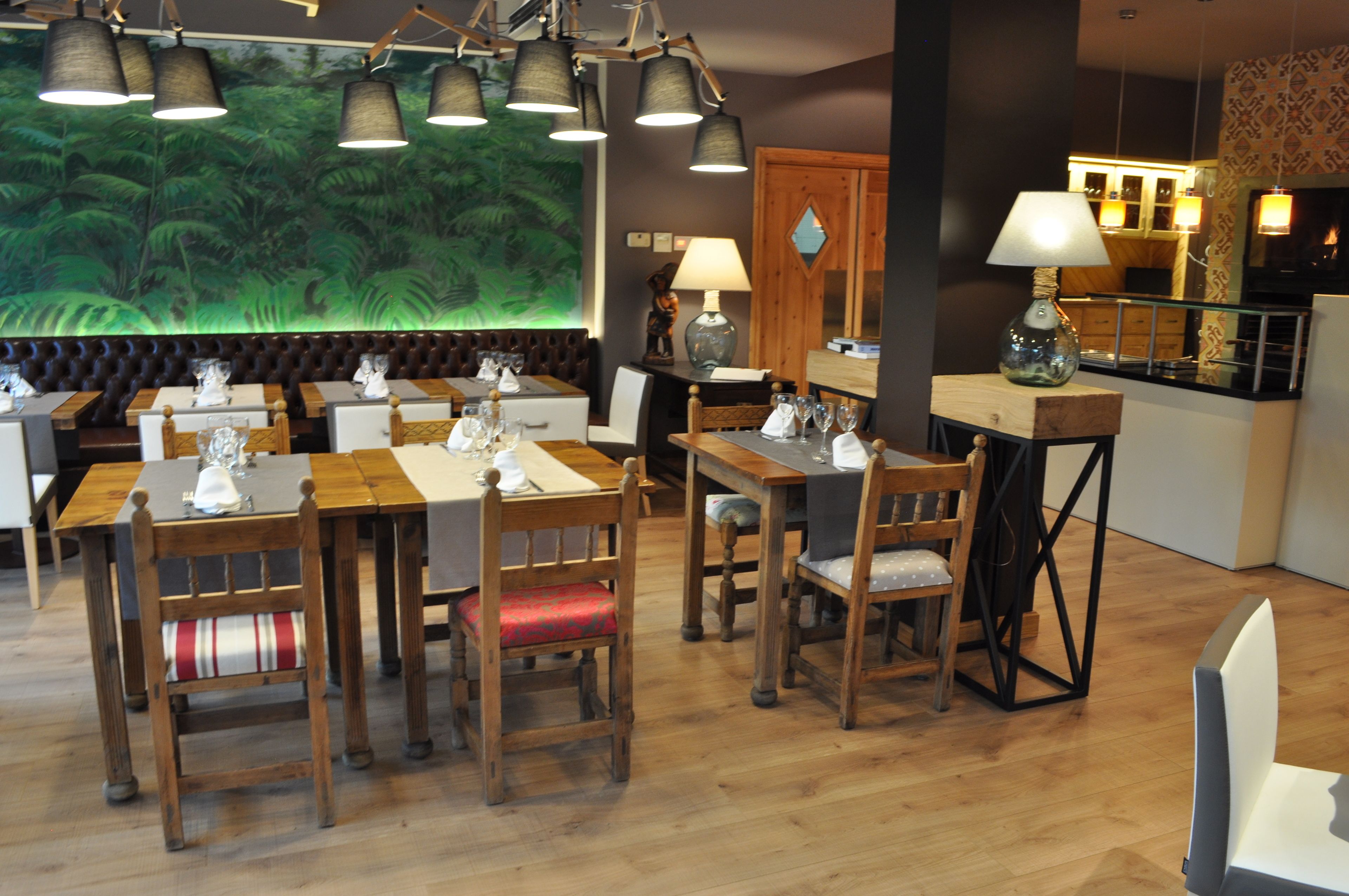 A restaurant with wooden tables and chairs, a large mural of a forest, and a bar area with a wooden counter.