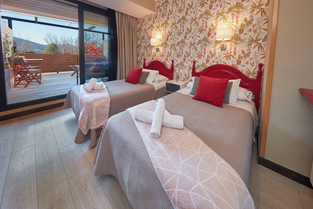 A hotel room with two beds, a balcony, and a view of the outdoors.