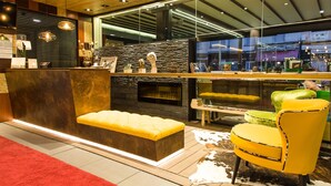 A modern reception area with a stone wall, a fireplace, and a seating area with yellow chairs. - Hotel Sánchez (Ainsa)