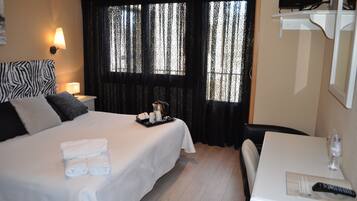 A hotel room with a bed, a table, a chair, a TV, and curtains.