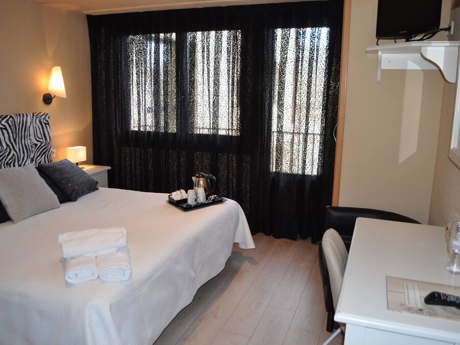 A hotel room with a bed, a table, a chair, a TV, and curtains.