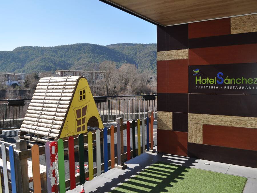 A hotel entrance with a colorful fence, a yellow playhouse, and a view of a forested hill.