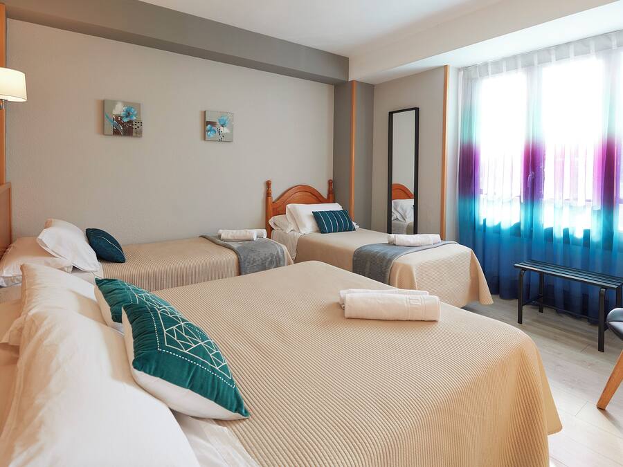 A hotel room with two beds, a bench, a mirror, and artwork on the wall.