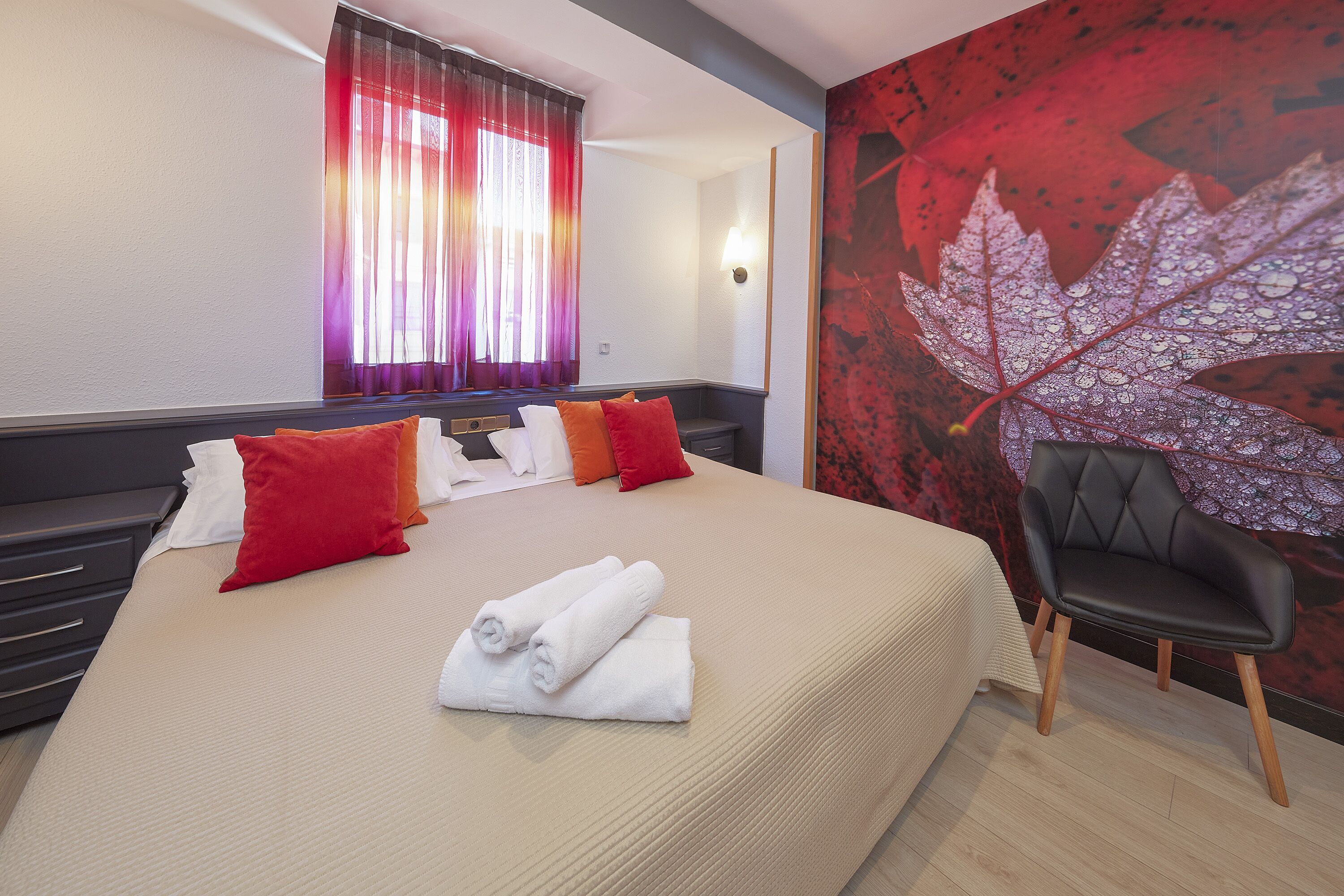 A hotel room with a bed, pillows, a chair, and a wall with a leaf design.