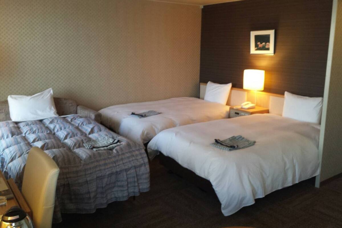 Una habitación de hotel con dos camas, un escritorio y una mesita de noche con lámpara.