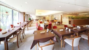 A hotel dining area with multiple tables and chairs, a reception desk, and a view of trees through large windows. - Hotel International House Osaka (Osaka)