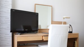 A hotel room with a wooden desk, a white chair, a flat-screen TV, a lamp, and a small refrigerator. - Hotel International House Osaka (Osaka)