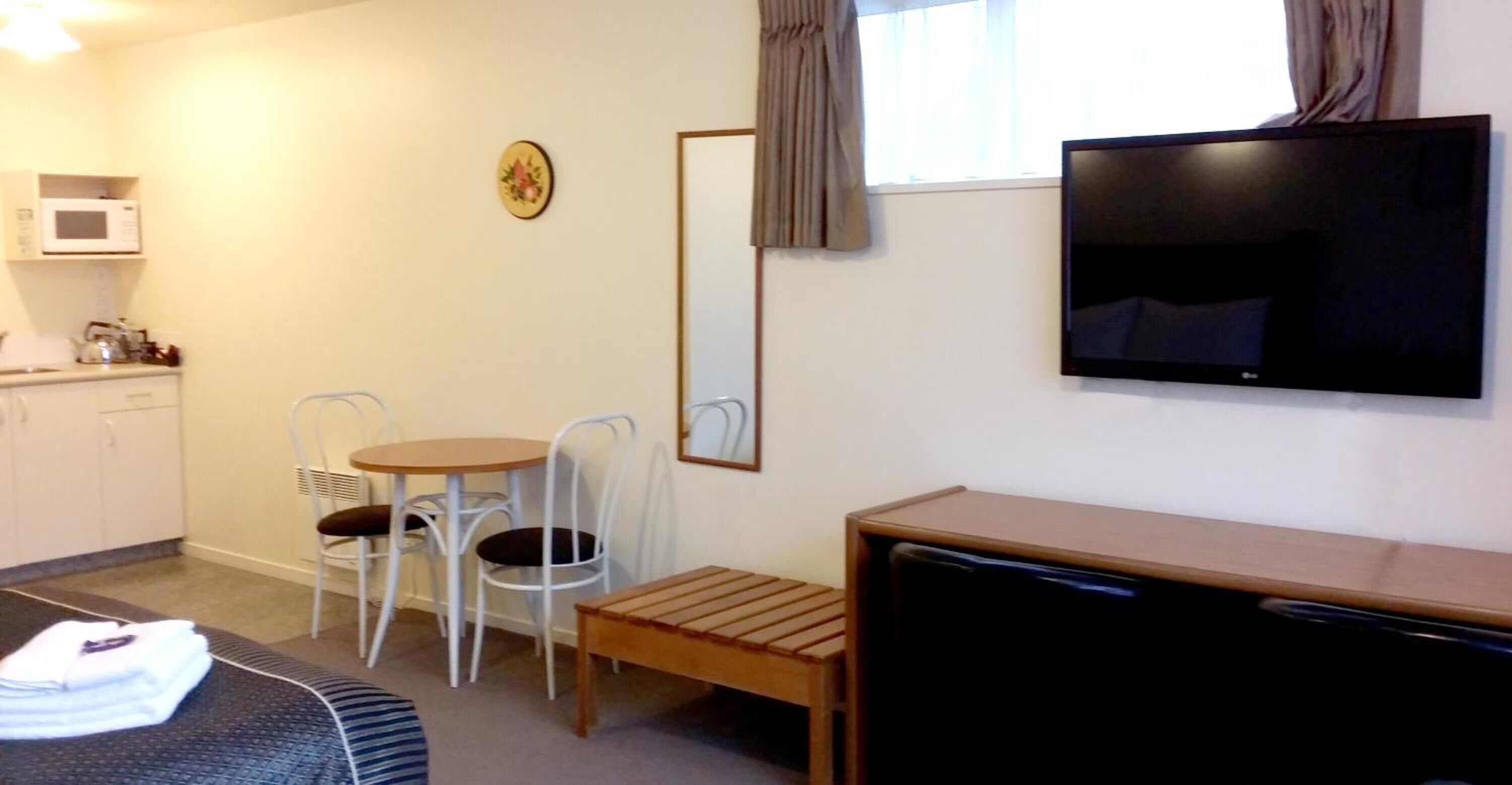 Ein Hotelzimmer mit einem Bett, einem Schreibtisch mit Fernseher, einem kleinen Tisch mit Stühlen, einer Mikrowelle und einem Fenster mit Vorhängen.