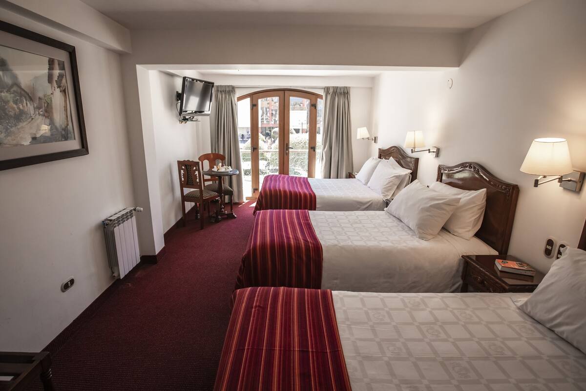 A hotel room with two beds, a TV, a chair, a table, and a balcony view.