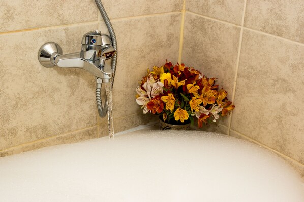 Rincón de baño con ducha, un arreglo floral y una bañera llena de agua.